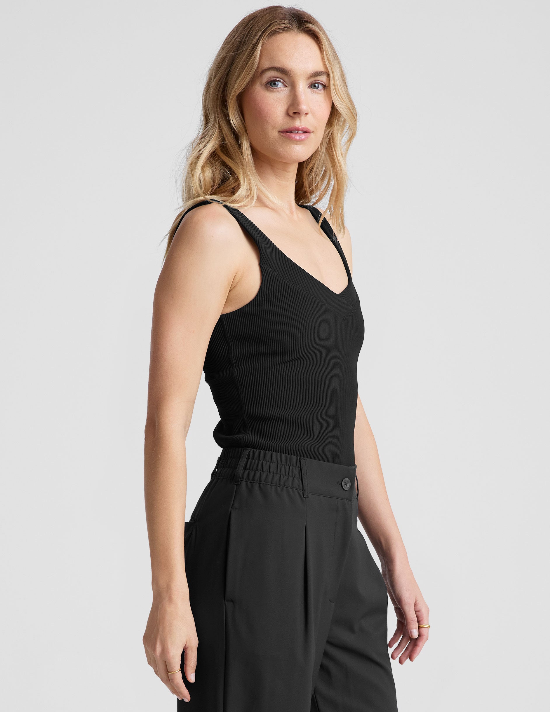 black ribbed tank top with a soft V neckline front and back, overlapping front neckline detail, and a performance lining shelf bra. Tank hits at a high hip length.