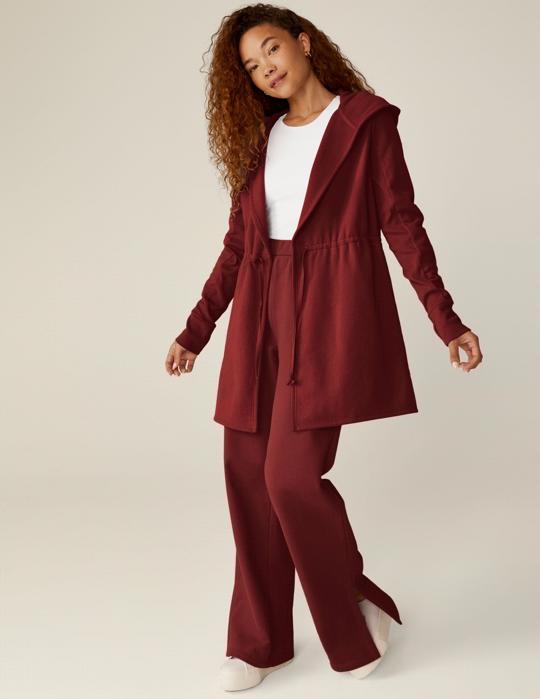 red long length hooded jacket with a drawstring at the waist and side pockets.