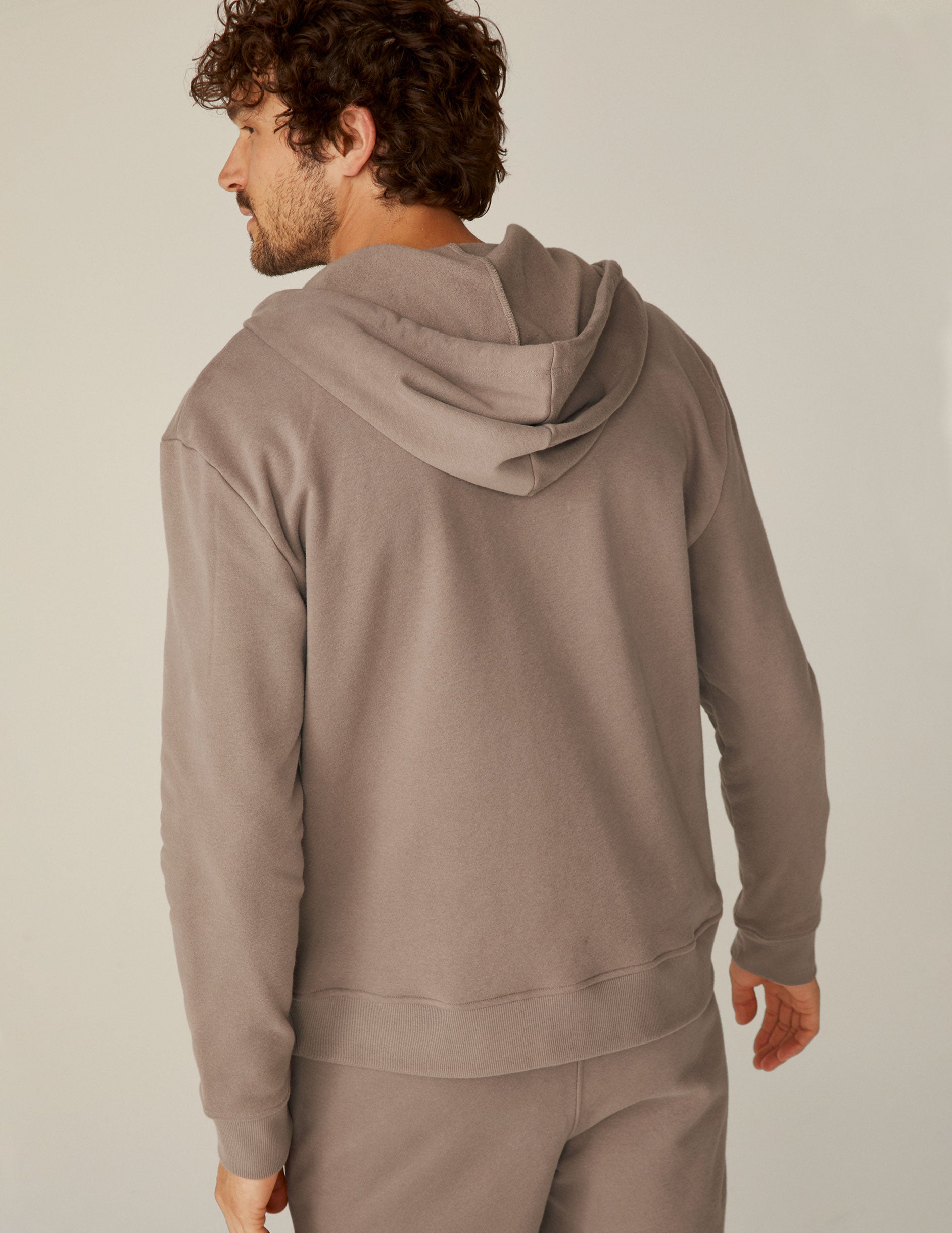 model is wearing a brown men's zip-up hooded jacket.
