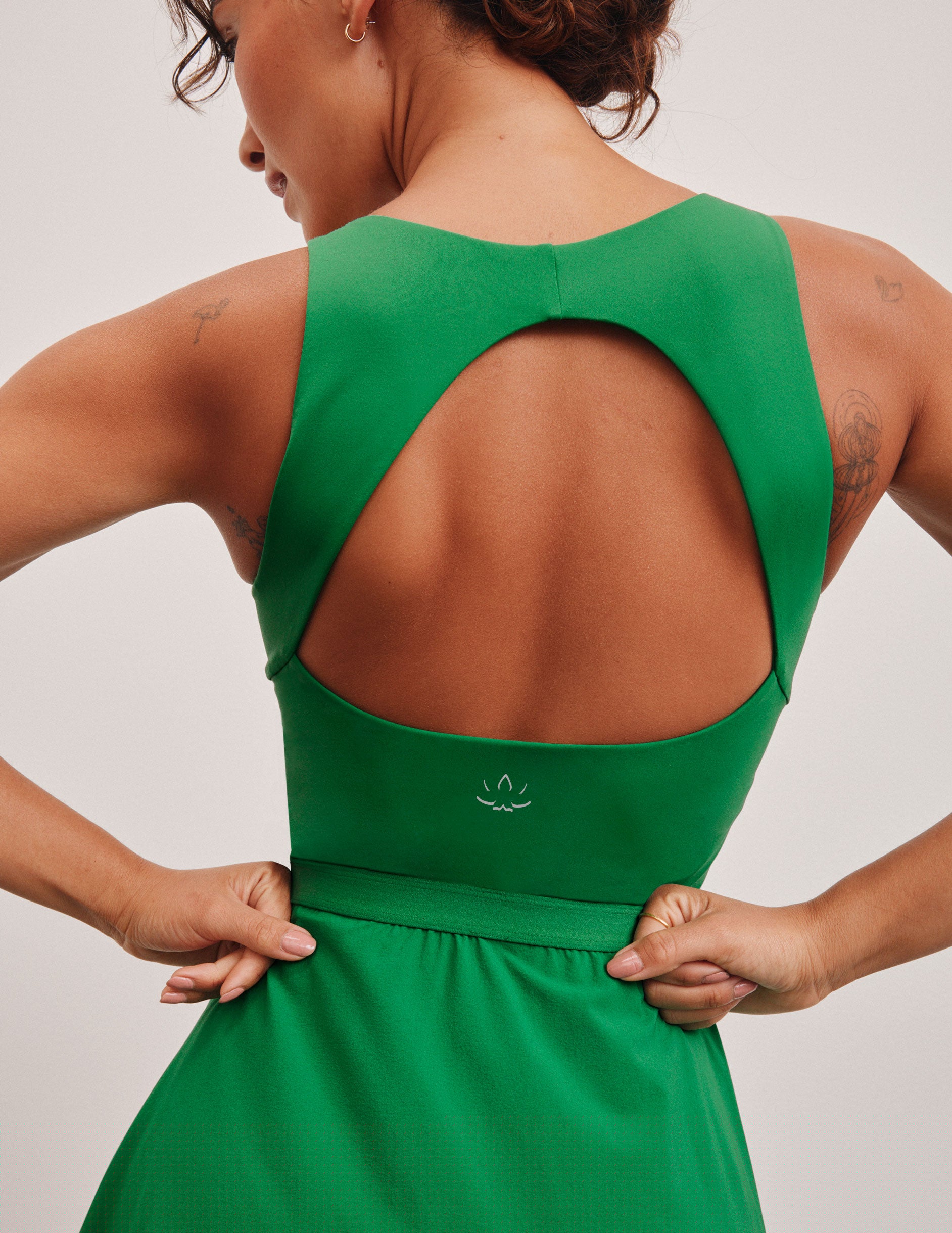 green mini dress in our stretch woven fabric with stitch down front pleats, a scoop front neckline, open back detail, bodice in performance stretch fabric, and skirt side vents for easy pocket access.