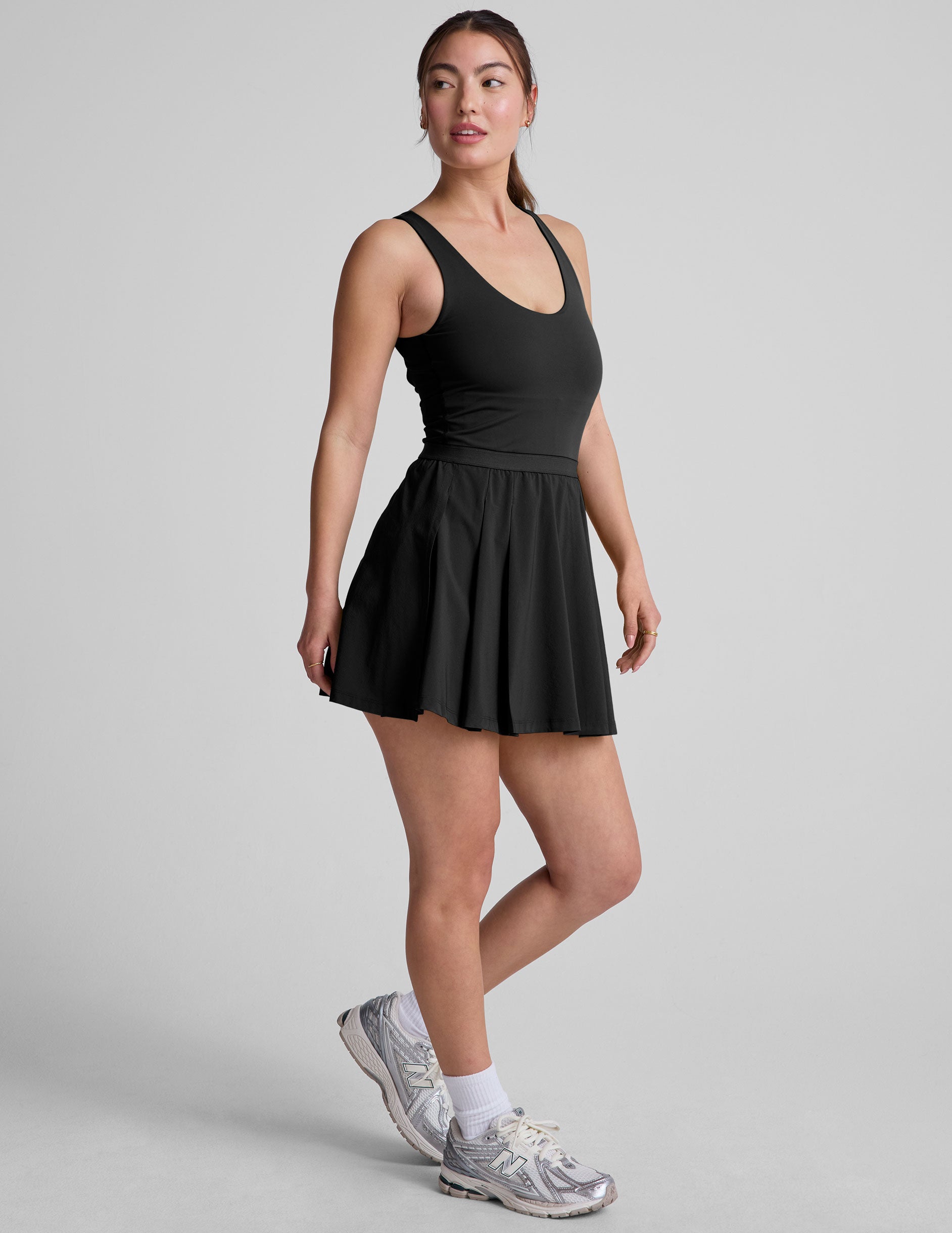 black mini dress in our stretch woven fabric with stitch down front pleats, a scoop front neckline, open back detail, bodice in performance stretch fabric, and skirt side vents for easy pocket access.