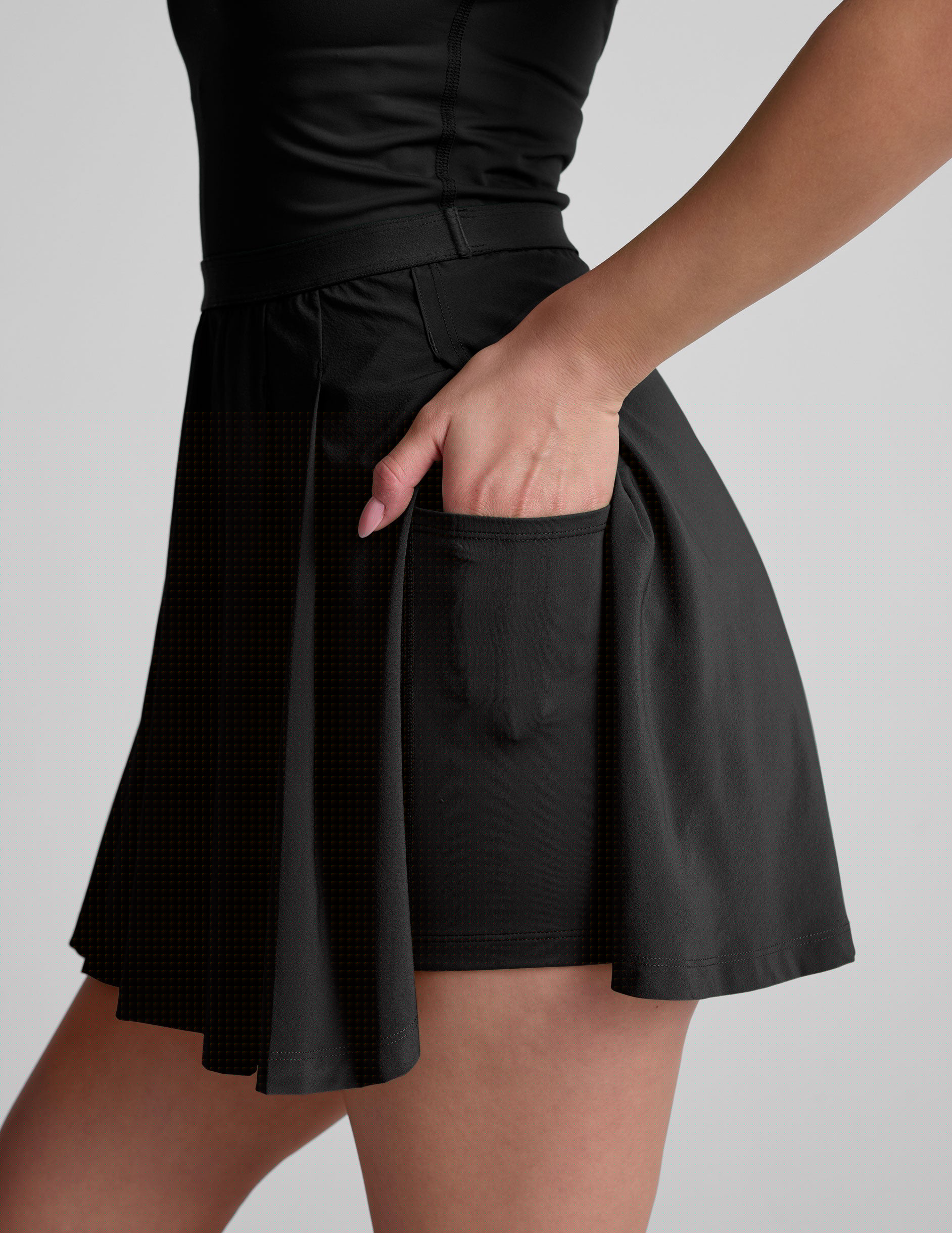 black mini dress in our stretch woven fabric with stitch down front pleats, a scoop front neckline, open back detail, bodice in performance stretch fabric, and skirt side vents for easy pocket access.