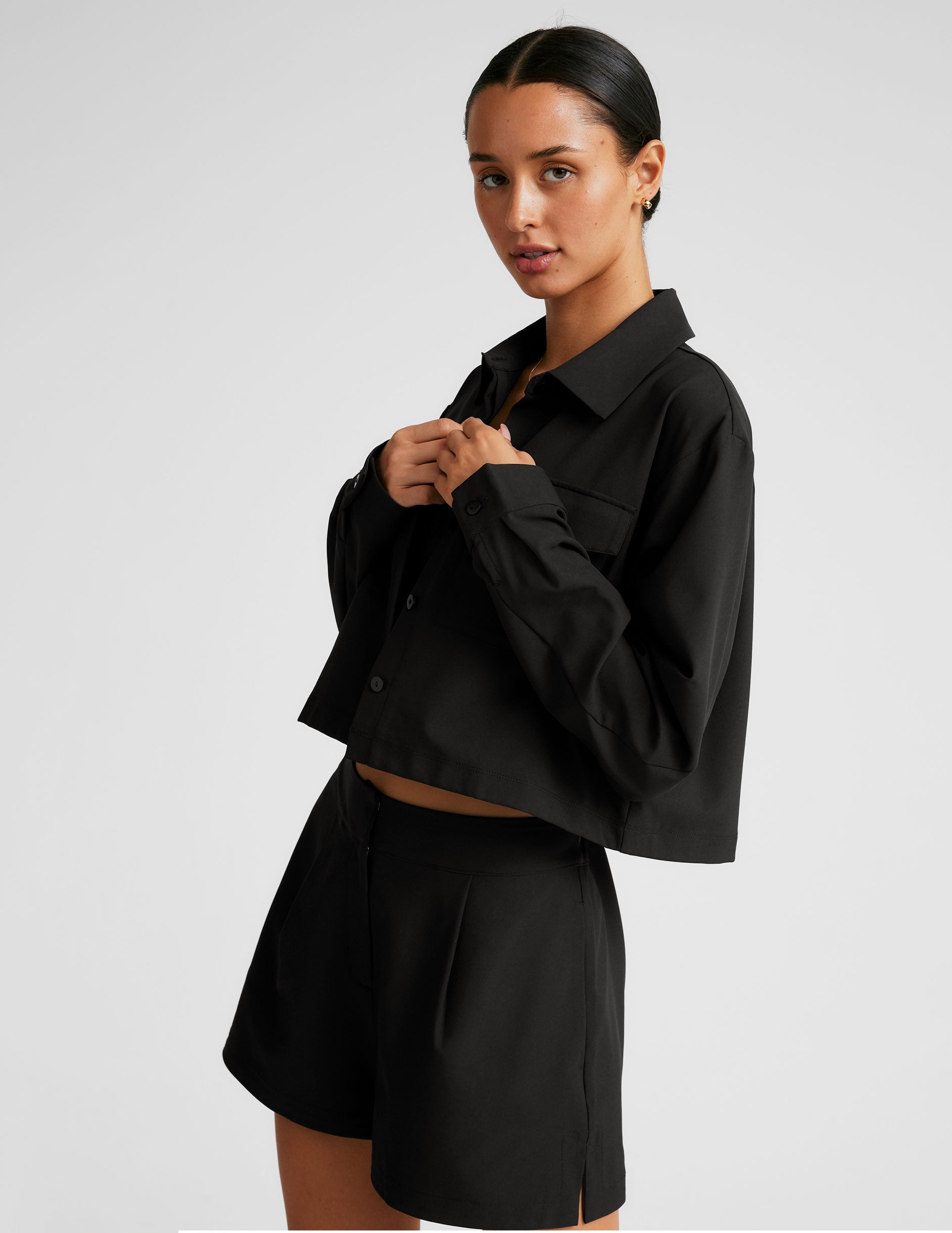 black cropped loose fitting jacket with a collar at neckline, hidden placket with button closure at center front, and front chest cargo pockets.