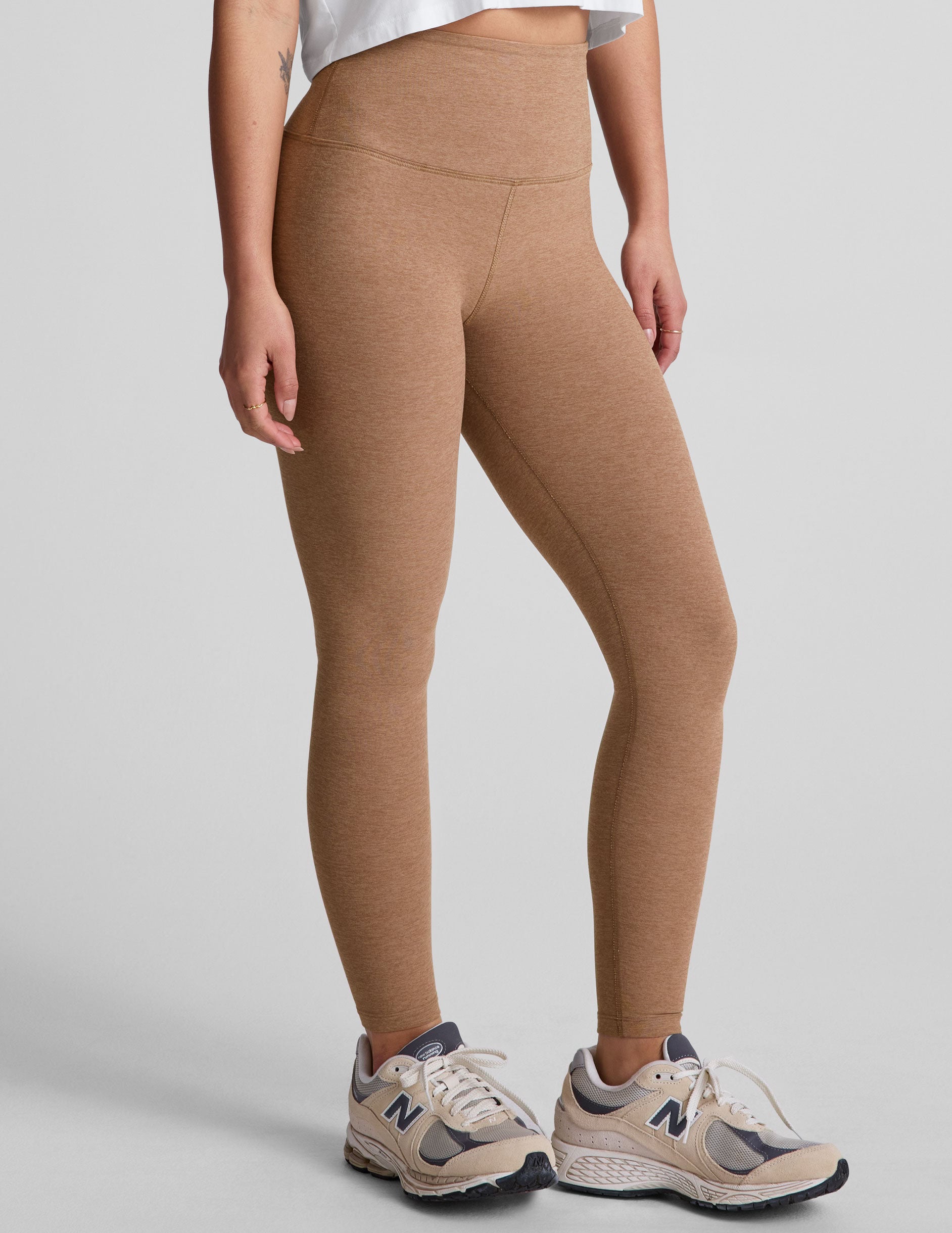 model is wearing brown high-waisted midi leggings and a white tank top.