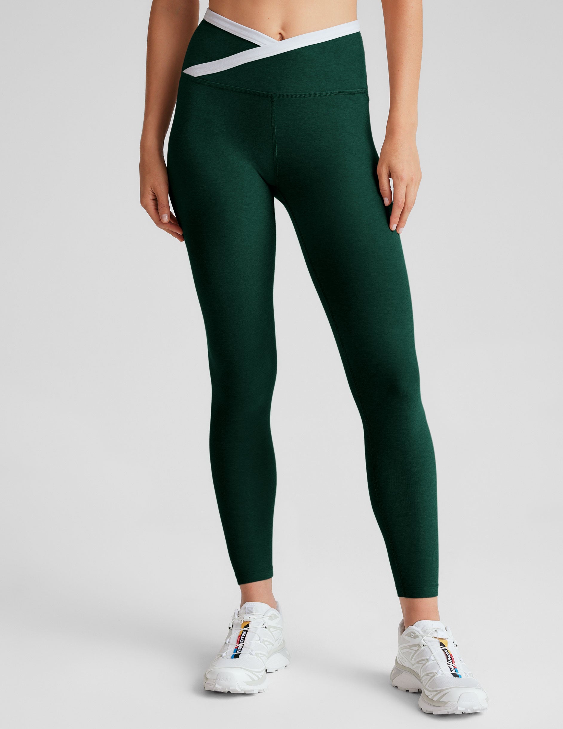 green high-waisted midi length legging with a crossover detail on the front waistband with white contrast binding along waistline.