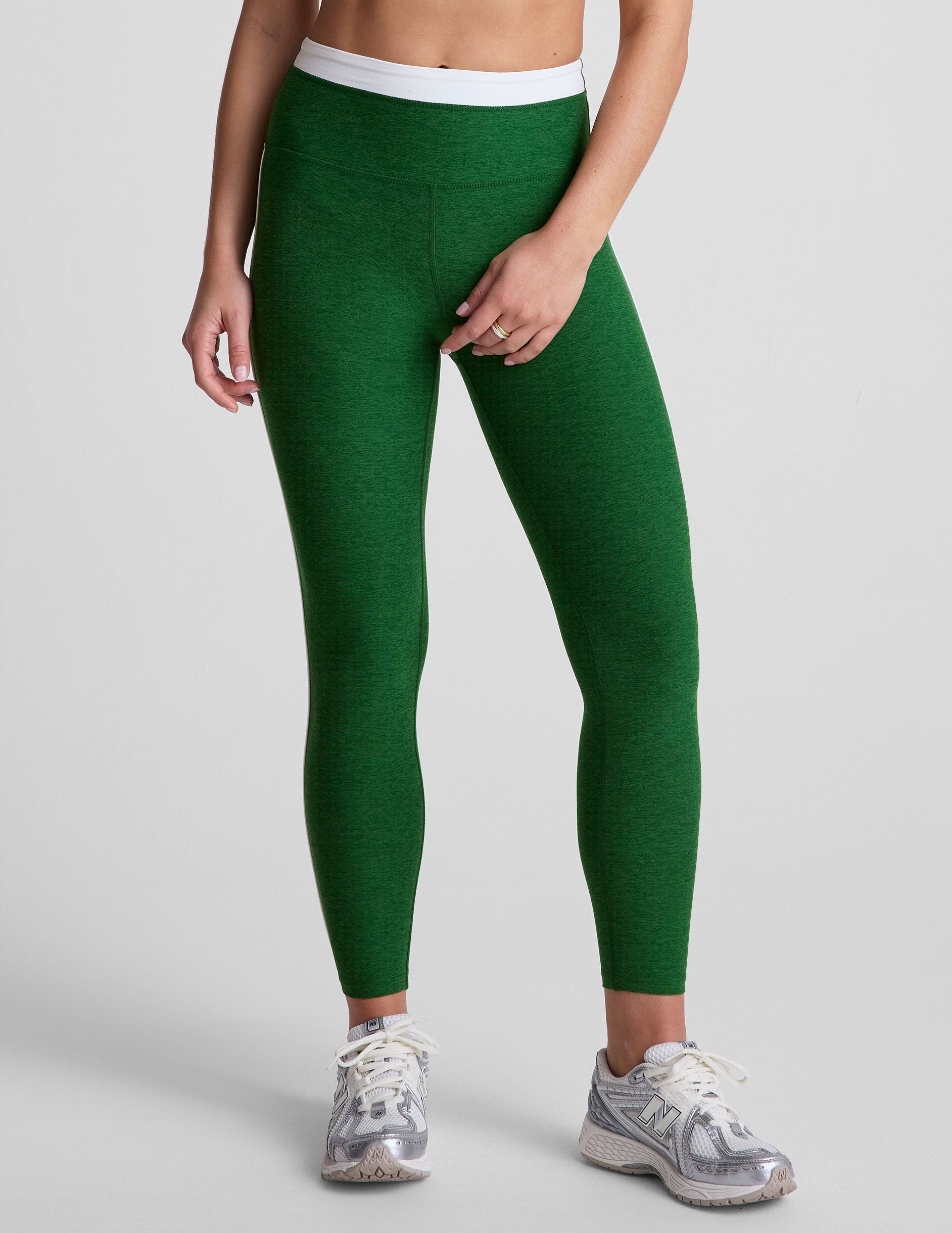 green high-waisted midi leggings with white contrast piping on side of leg and around waistband.
