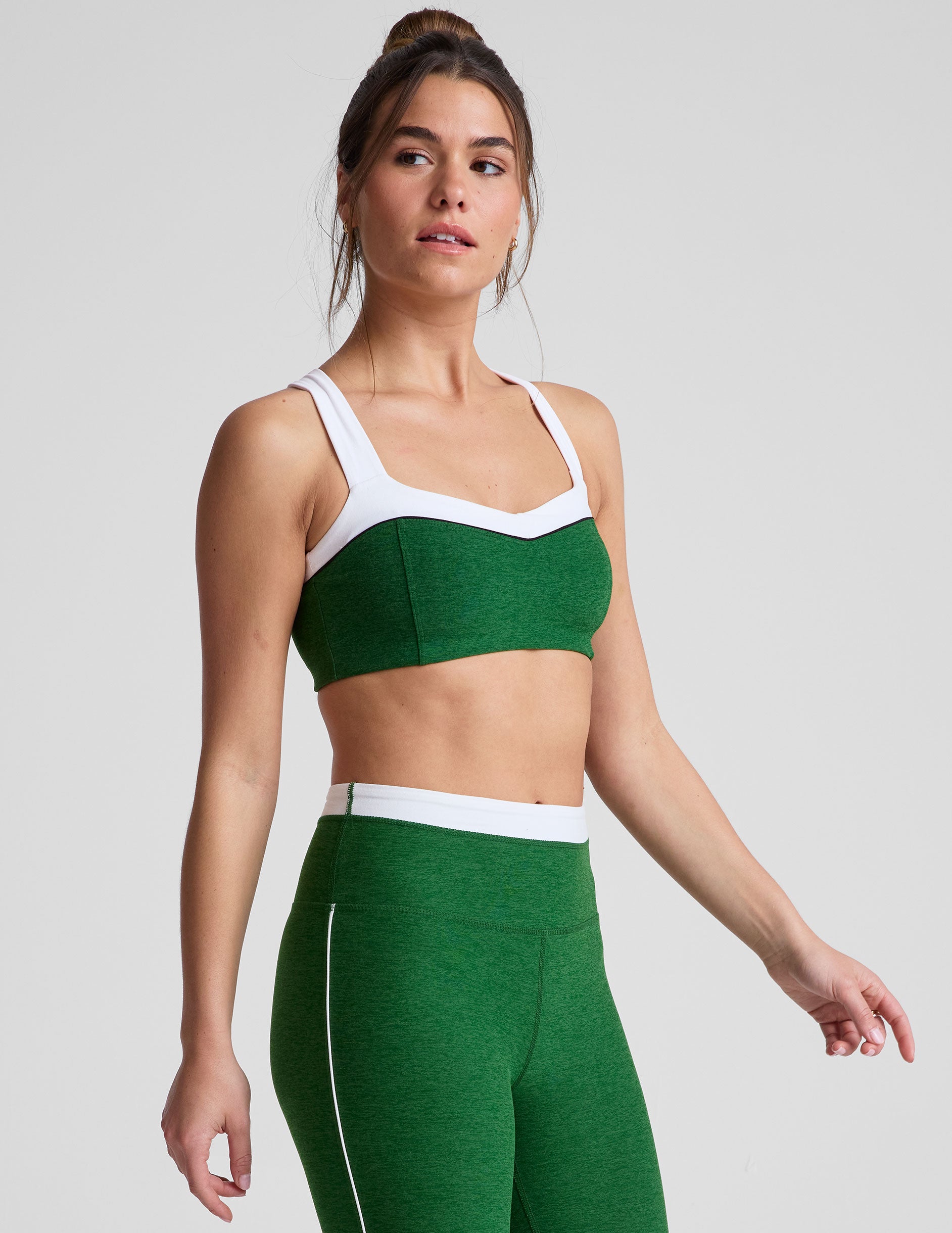 side view of green self-lined, medium to low support bra top with a colorblock sweetheart neckline panel, contrast straps, and princess seams. bra is paired with green high-waisted midi leggings with a white contrast trim around waistband and down sides of legs.